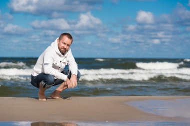 Beyaz kazak beac üzerinde çömelme giyen sakallı genç adam