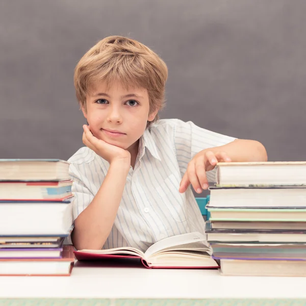 Çocuk başını bir yandan kalın kitaplarla dolu bir masada yaslanmış