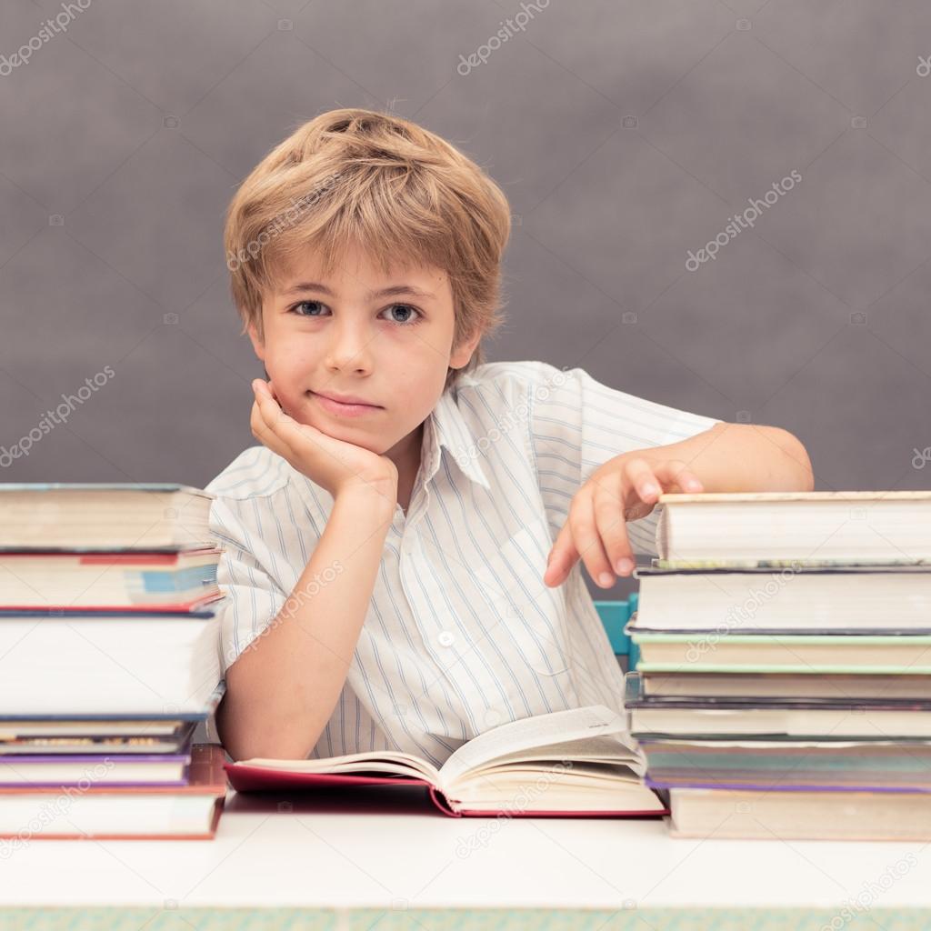 Boy leaning his head on a hand  at a table full of thick books