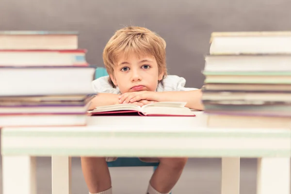 Genç çocuk bir masa dolusu kitap yaslanmış