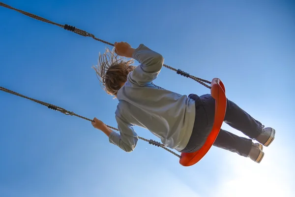 Boy swinging very high, blue sky in background — Stock Photo, Image