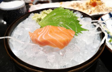 Somon balığı taze çiğ bir parça kesmek yeşil oba yaprağı ile Japon lezzeti ve siyah kasede buzda wasabi..