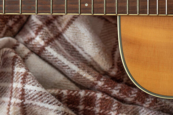 dark neck guitar without strings with frets of light wood on a woolly brown warm cage plaid