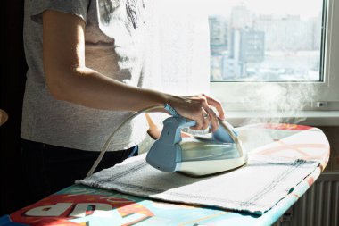 Kadın ütü masasındaki elbiseleri ütülüyor. Ev işleri, karantina