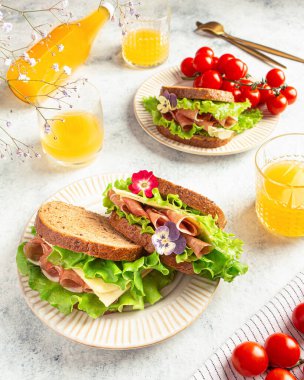 Jambonlu sandviç, peynir ve gri arka planda marul yaprakları. Ev yemeği.