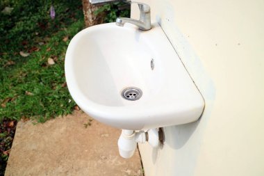 Beyaz lavabo bir bahçe fotoğrafında duvara dayanıyor.