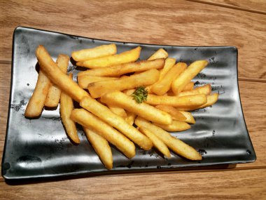 Siyah kare bir tabakta servis edilen kurutulmuş patates kızartması.