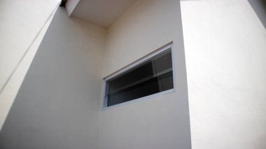 Pürüzsüz beyaz yüzeyler ve küçük uzun pencereli temiz, modern bir bina cephesi.