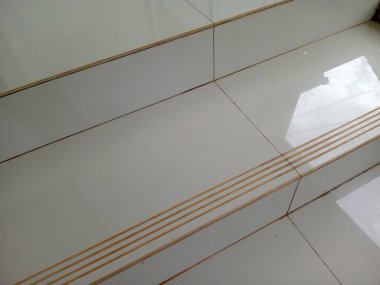 Beyaz fayanslı merdiven basamağı, anti kayma kanalları ve güneş ışığı yansıması, iç mimari detay minimumu..