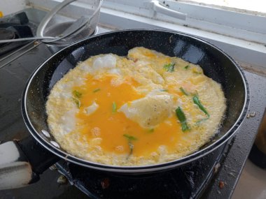 Gaz sobasında siyah tavada pişen yumurtalar, akışkan yumurta sarısı ve yeşil sebzeler, mutfakta yakın pişirilen ev yemekleri..