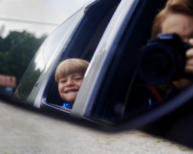 Pencereden bakan çocuk ve ön koltuktan fotoğraf çeken kadın..