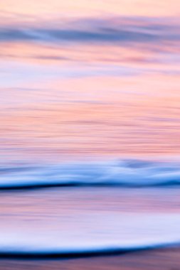 Denizin soyut manzarası. Doku suyu, gökyüzü ve kum tropikal günbatımı renklerinde bulanık hareket ediyor