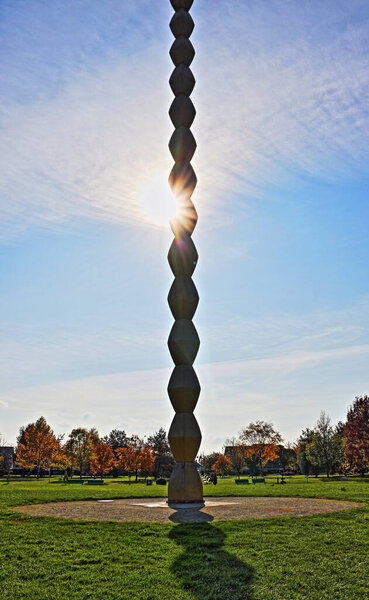 Targu Jiu, RO - November 7, 2020: Endless Column from the Sculptural Ensemble of Constantin Brancusi. Homage to the Romanian heroes of WW 1. UNESCO world heritage monument. Artistic view point with sun halo. Cultural tourism destination.