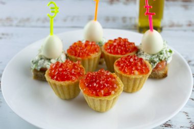 Kırmızı havyarlı kanepeler, beyaz tabakta somon ve bıldırcın yumurtası, tartlar, şişte küçük iştah açıcı sandviçler, ahşap zeminde krem peynirli ekmek.