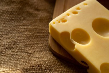 Bir parça maasdam peyniri, lezzetli peynir ve mantarlar kesim tahtasının üzerinde çuval bezi arka planında