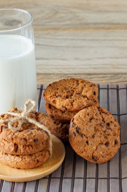 Kabartma kağıdının üzerinde çikolatalı kurabiye yığını, hafif ahşap arka planda bir bardak süt..