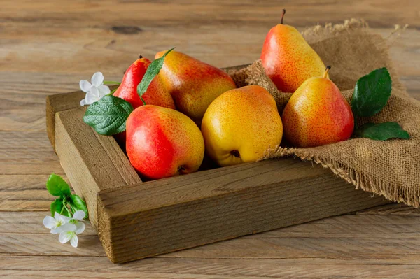 fresh pears with leaves in a wooden box on wooden background.