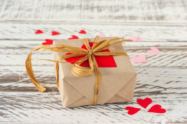 Sanatsal kağıt hediye kutusu, kordon yayı ve ahşap arka planda kırmızı kalpler. Sevgililer günü ve doğum günü için kutlama kartı..