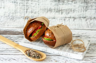 Avokado ve domatesli sağlıklı somon burgeri ahşap arka planda el işi kağıt ile servis edilir.