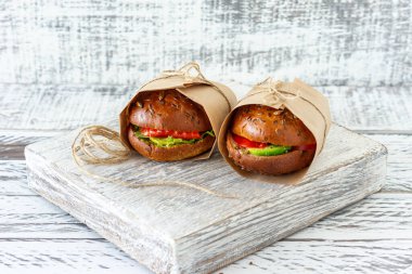 Avokado ve domatesli sağlıklı somon burgeri ahşap arka planda el işi kağıt ile servis edilir.