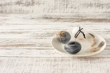 Koyu renklerde renkli Paskalya yumurtaları ve ahşap masadaki bir tabakta tüyler. Paskalya tatili için hazırlık. Fesstive bileşimi