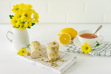 Şam fıstıklı helva beyaz ahşap masa üzerinde çiçekler ve çay ile servis edilir..