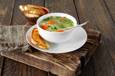 Beyaz kasede sebzeli tavuk çorbası. Ahşap arka planda lezzetli ev yapımı et suyu..