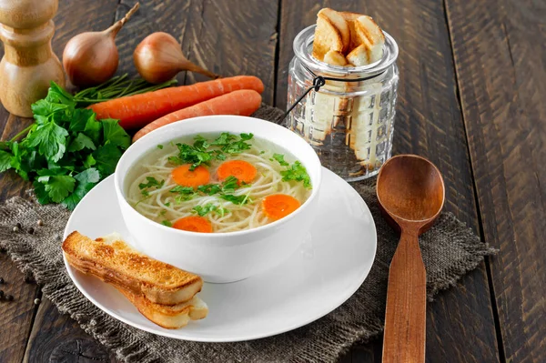Chicken bouillon with noodles and carrot slices on a wooden table in rustic style.