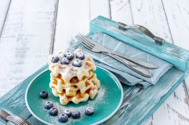 Kahvaltıda ahşap tepside servis edilen yabanmersini ve şeker tozlu ev yapımı Belçika waffle 'ları.