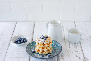 Ev yapımı vanilyalı waffle, şeker tozu ve yabanmersini tabakta, mükemmel bir aile kahvaltısı..
