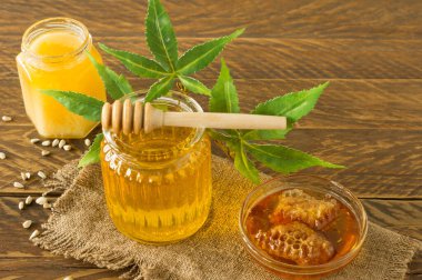 Ballı kavanoz dolusu taze CBD bal ahşap masa üzerinde kenevir yapraklı yakın plan.