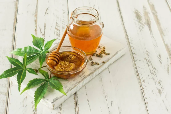 Cannabis honey in a bowl with wooden deeper, hemp leawes amd seeds on wooden table.