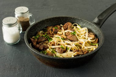 Maydanozlu pişirme kaleminde soğanlı tavuk ciğeri ve spagetti. Lezzetli bir aile yemeği..