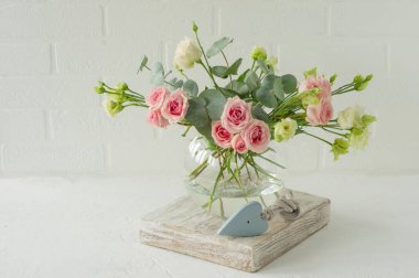 Bir buket gül, östoma ve okaliptüs cam bir vazoda masanın üstünde. İç dekorasyon için çiçek bileşimi