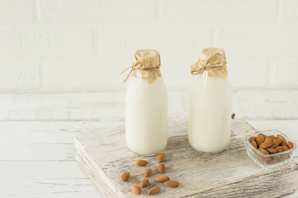 Homemade Almond milk in glass bottles with almonds on wooden table.