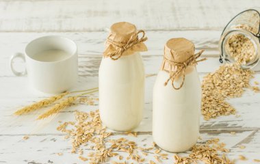 Cam şişelerde yulaf sütü ve tahta bir masada yulaf ezmesi.