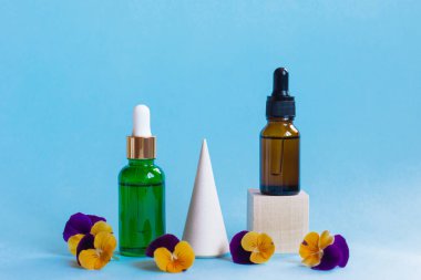 Pipetli serum cam şişeler ve mavi arka planda güzel viyola çiçekleri. Doğal Organik Spa Kozmetik Konsepti. Ön görünüm