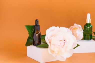 Tıbbi ve kozmetik kullanım için iki cam damlatıcı şişesi ve açık bej arka planda beyaz çiçek. Cilt bakımı ve SPA kavramı