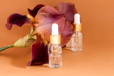 Cilt bakımı için çiçek özlü serum. Yüz ve vücut bakım spa konsepti. Doğa kozmetik ürünleri cam şişede pipetle ve pembe süsen çiçekleriyle bej arka planda.