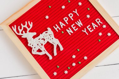 Kırmızı keçeli mektup tahtası mutlu yıllar ve beyaz arka planda beyaz geyik ve şeker filizi. Kış tatili için kutlama kartı..