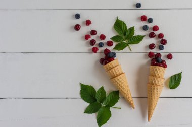 Taze yaban mersini, kiraz ve ahududu waffle külahında ahşap beyaz arka planda. Üst görünüm.