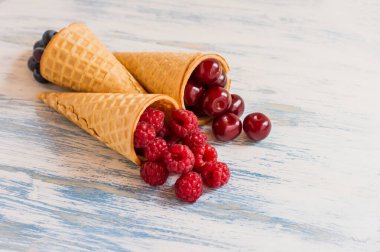 Ahududu, kiraz, ahşap beyaz ve mavi arka planda yabanmersinli üç waffle boynuzu. Yaz tatlısı. yan görünüm