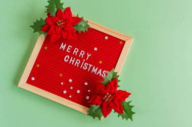 Minimalizm tarzında mutlu noel tebrik kartları. Yeşil arkaplanda kırmızı piosentia çiçekleri olan mektup panosu.