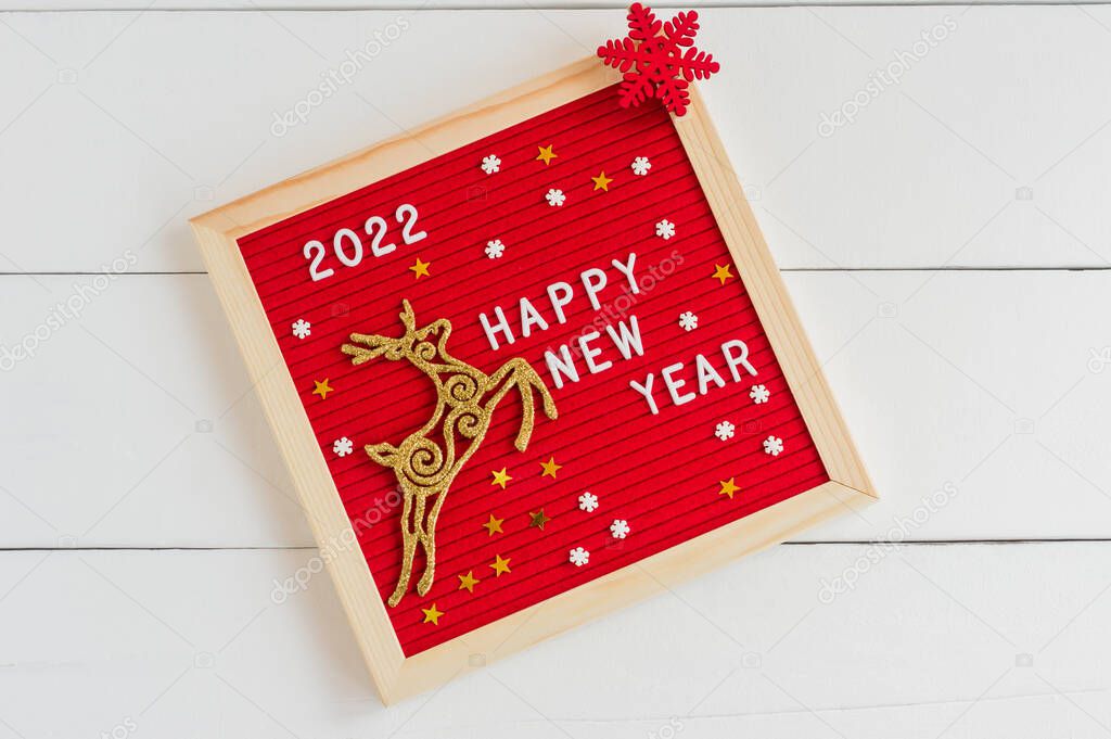 Happy new year 2022. Letter board with golden deer and red flake on a white background. Flat lay