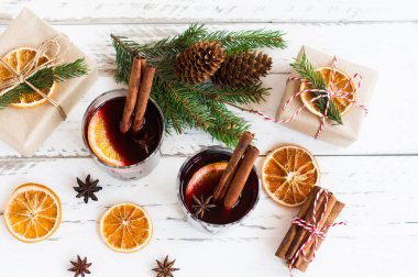 Kutlama kartı, sıcak şarap, paketlenmiş hediye kutuları ve beyaz masada geleneksel baharatlar..
