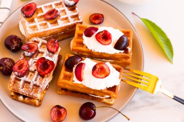 Bir tabak taze Belçika waffle 'ı ve beyaz bir masada kremalı kiraz.