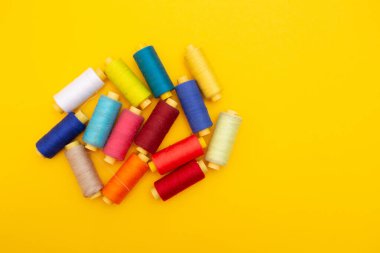 Sarı arkaplan üzerindeki renkli iplik bobinlerinin üst görünümü, dikiş, metin için yer