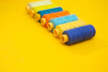 Sarı arkaplan üzerindeki renkli iplik bobinlerinin üst görünümü, dikiş, metin için yer