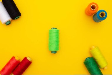 Sarı arkaplan üzerindeki renkli iplik bobinlerinin üst görünümü, dikiş, metin için yer