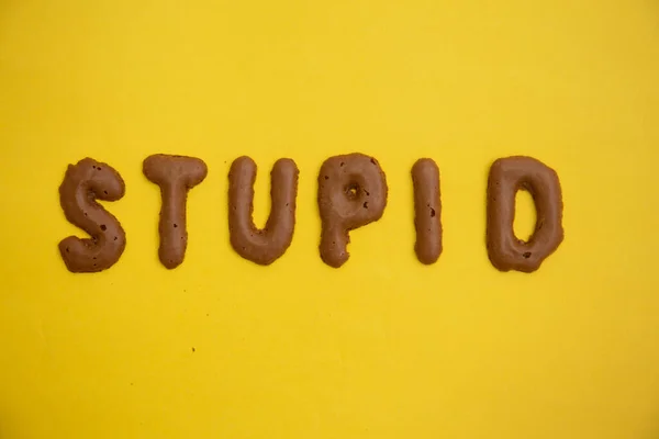 WordのStupidは 黄色のテーブルの上に自家製チョコレートクッキーアルファベットから配置 — ストック写真
